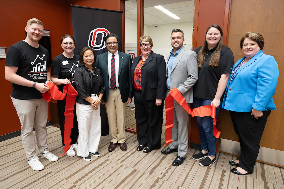 A group of 8 people smile and hold a freshly cut large red ribbon to commemorate the opening of the Maverick Headshot Studio