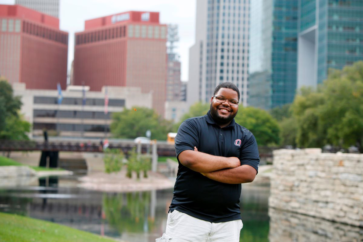 man standing in front of pond with city skyline behind him