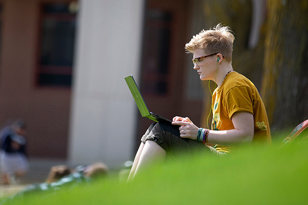 student sitting in the grass on a sunny day using a laptop