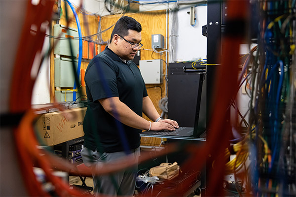 I.T. technician working on a terminal in a server room crammed with hardware and wiring