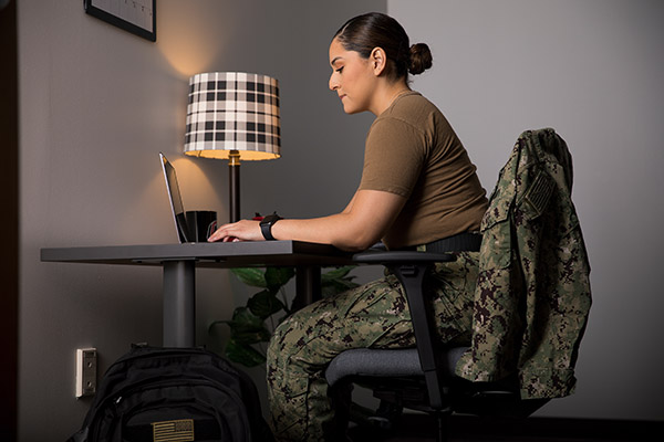 person in military fatigues sitting at a small table using a laptop