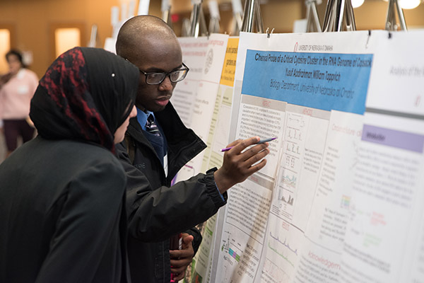 two people closely reading a research poster with of them pointing to a particular detail