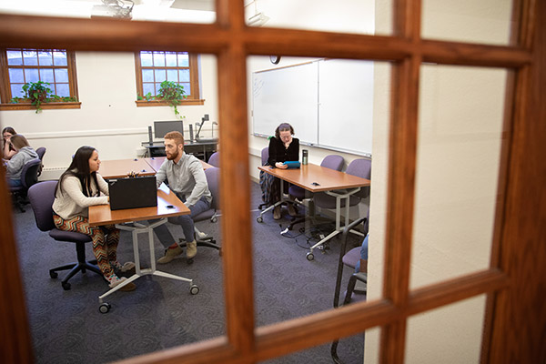 view through a window into a room filled with people sitting at tables in pairs