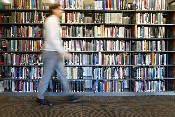 person walking past shelves of library books