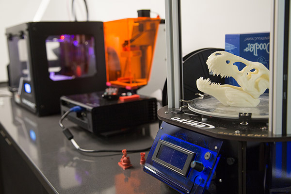 row of 3D printers on a countertop with various prints completed or in progress