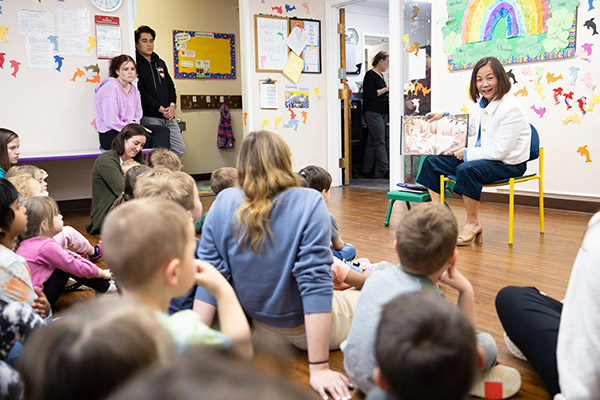 classroom full of small kids sitting on the floor listing to chancellor li read them a story from a book