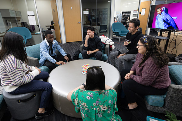 multiple students seated around a large round table playing a card game