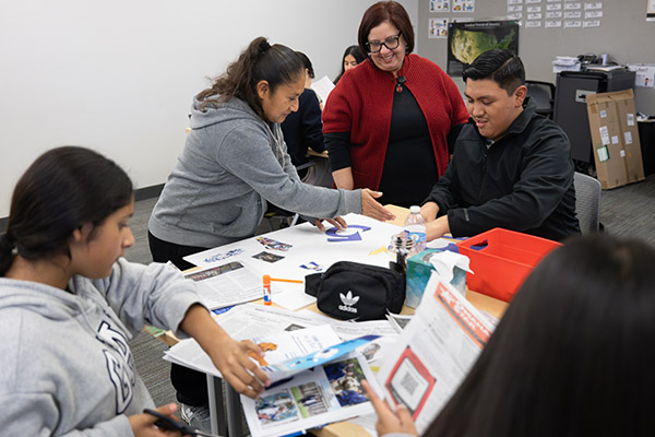 students at a table with colorful materials working together as an instructor looks on