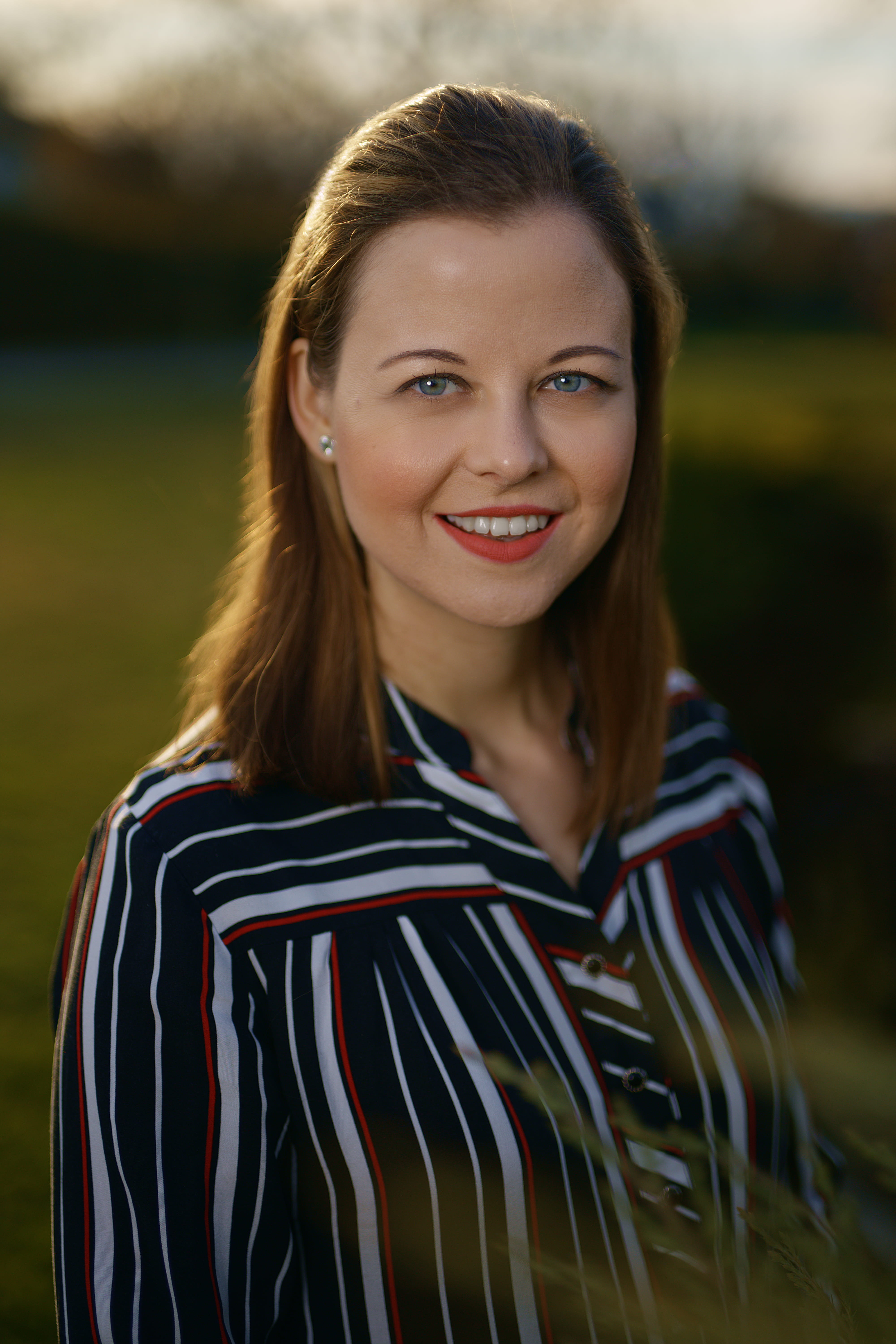 Smiling woman in a striped blouse, photographed outdoors with a softly blurred background.