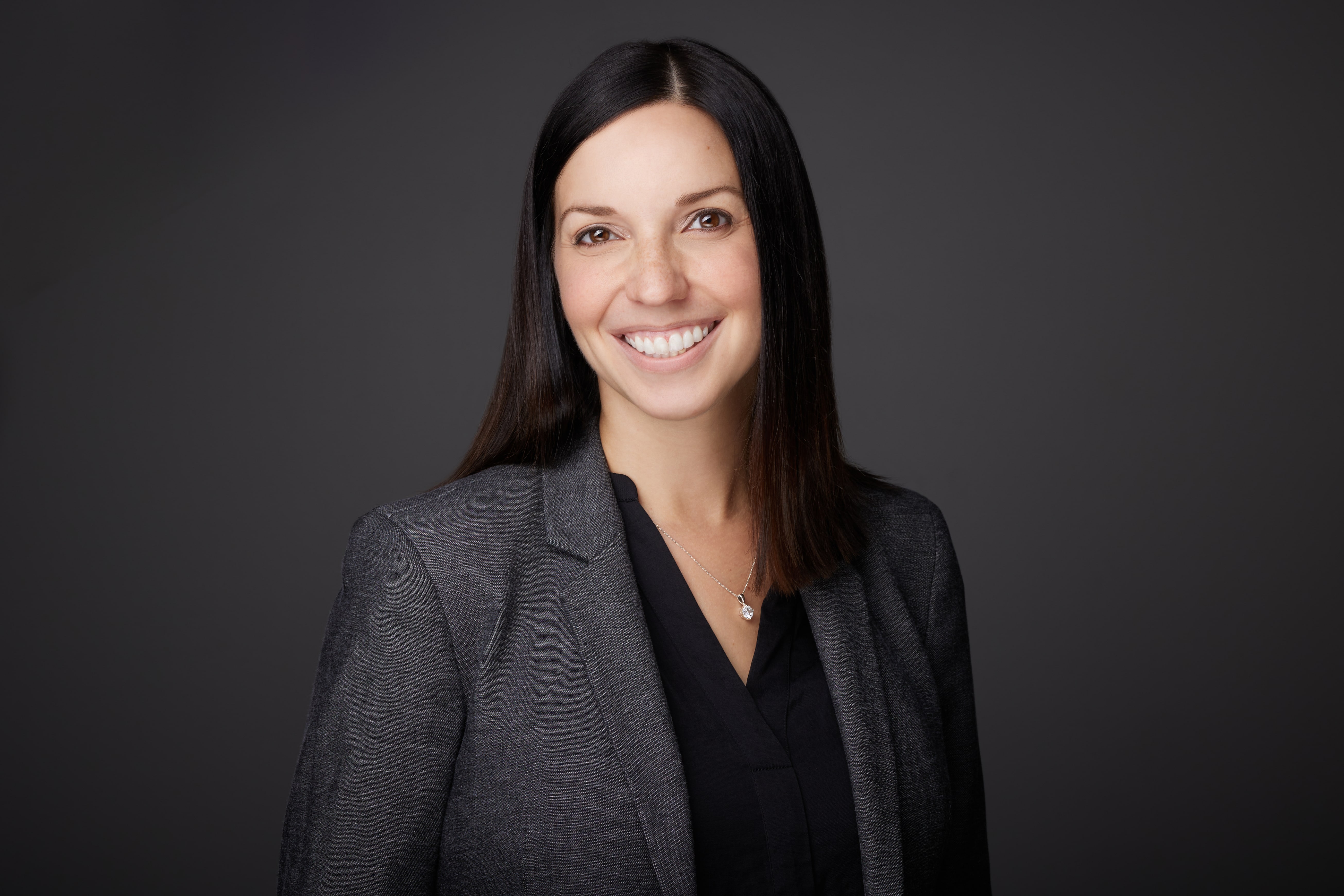 a woman with straight dark hair and a gray jacket smiles at the camera
