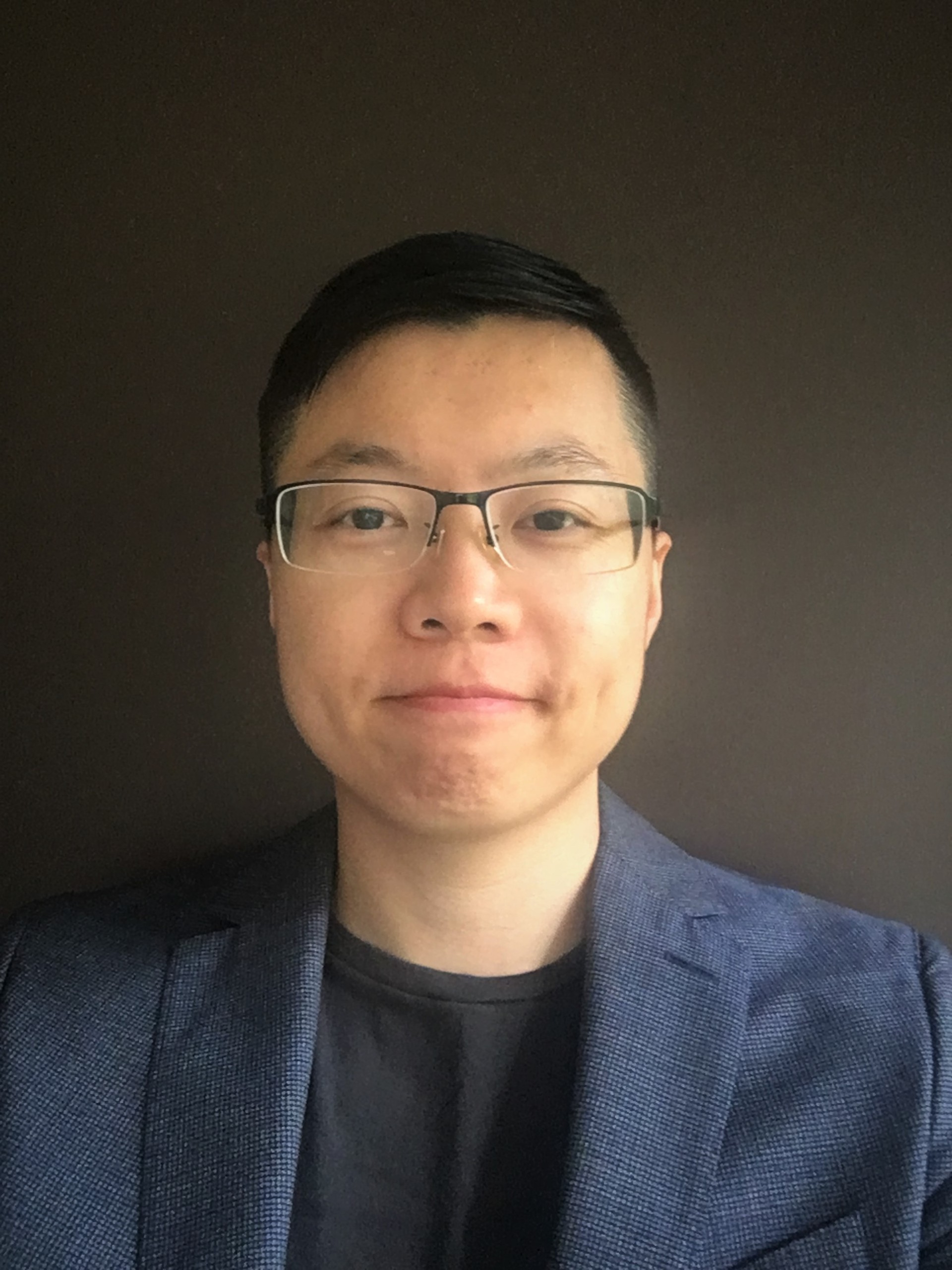 a man wearing glasses and a dark suit looks at the camera