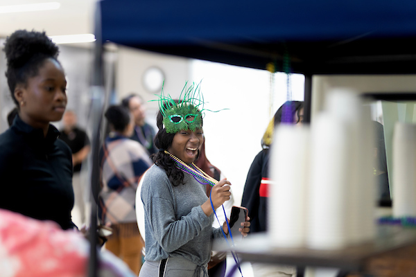 a student smiles at the camera as she holds a green mask celebrating mardi gras at uno