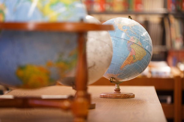 "Close-up of several globes on a wooden table, with a focus on South America. Bookshelves are visible in the blurred background