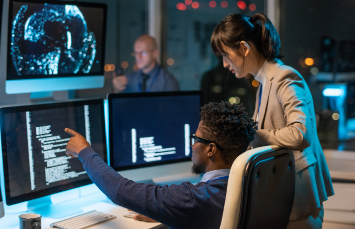 Two cybersecurity professionals analyzing code on multiple monitors in a dimly lit, high-tech office environment