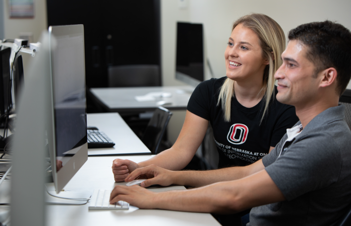 Two students working together on a computer in a university lab, with one wearing a university-branded shirt.