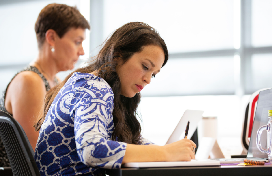 A focused female student taking notes in a classroom setting, representing academic engagement and professional learning.