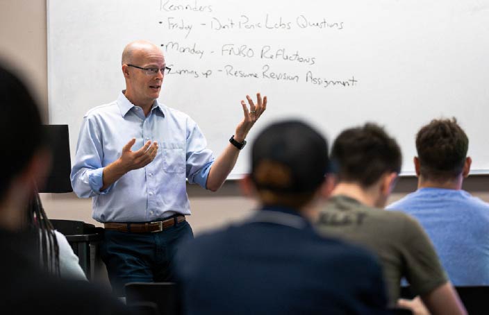 A professor gestures while teaching a class of students, highlighting the hands-on, faculty-led learning environment in the Management Information Systems program.