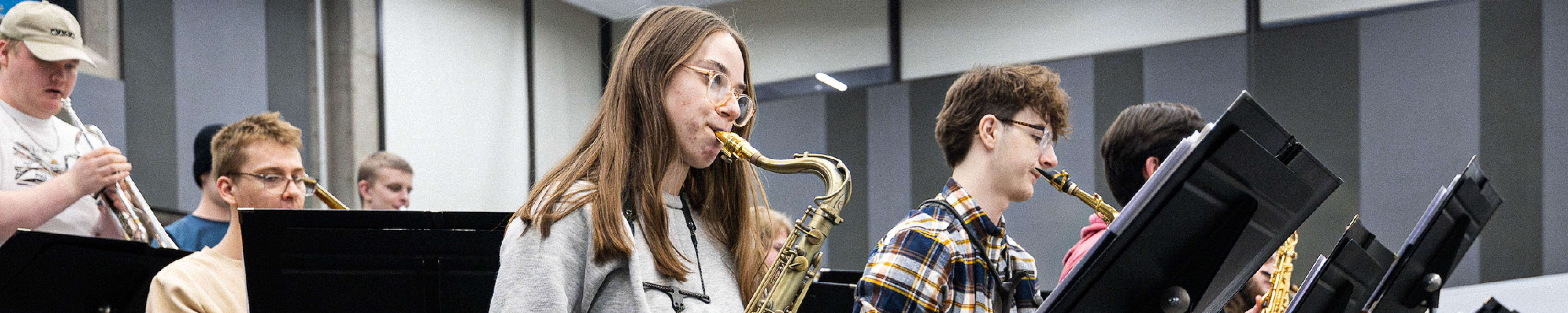 Students playing saxophones and other instruments during a music ensemble rehearsal.