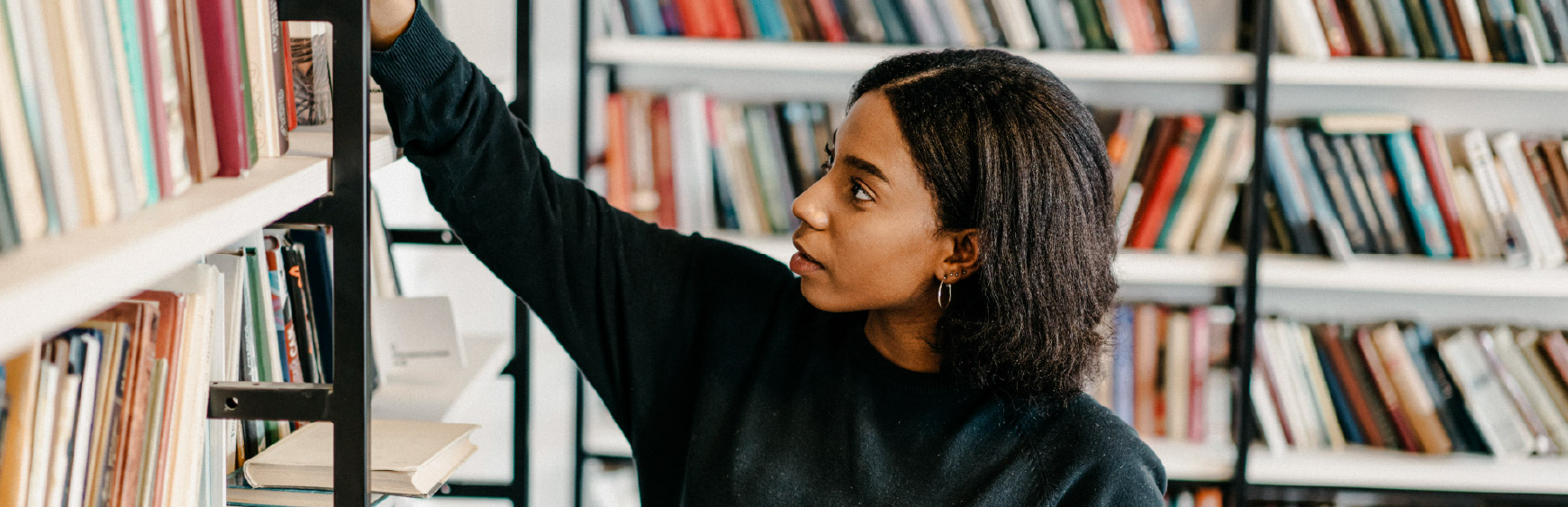 Student reaching for a book on a library shelf