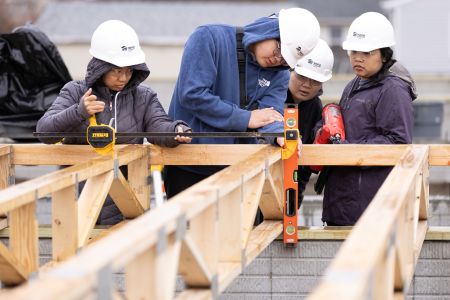 Students working on measuring and leveling wooden framing for a house.