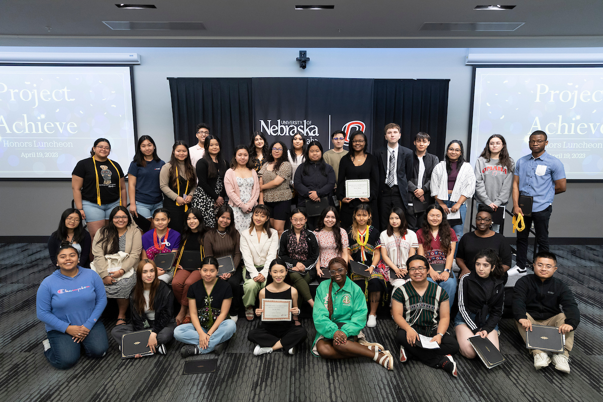Group photo of university students at a graduation recognition ceremony, posing together with certificates and honors cords.
