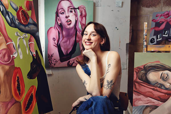 A student sits in an art studio surrounded by colorful paintings.