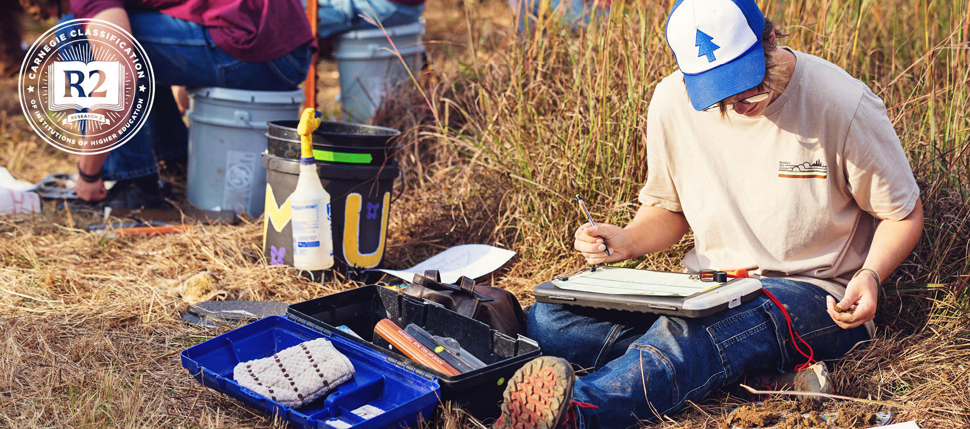 student wearing gloves and a cap works outdoors with research equipment.