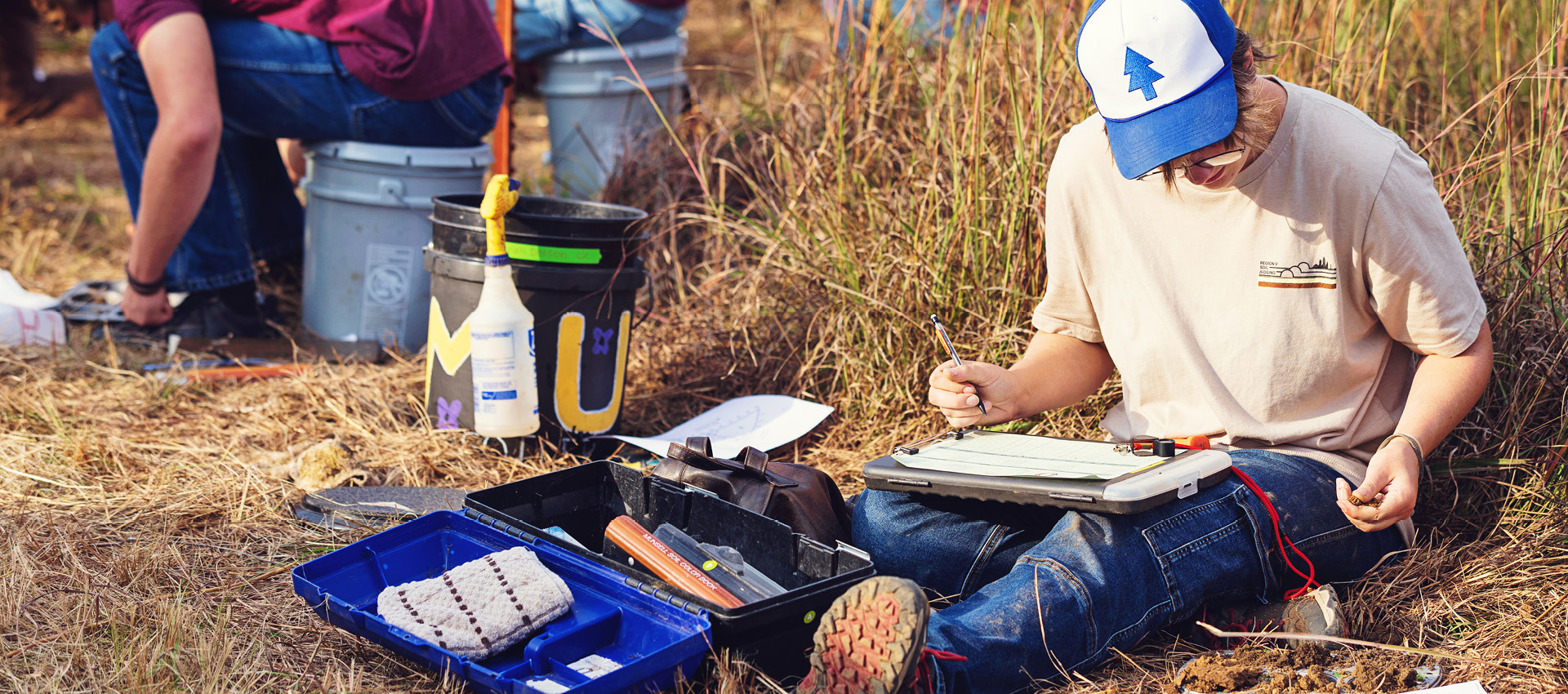 student wearing gloves and a cap works outdoors with research equipment.