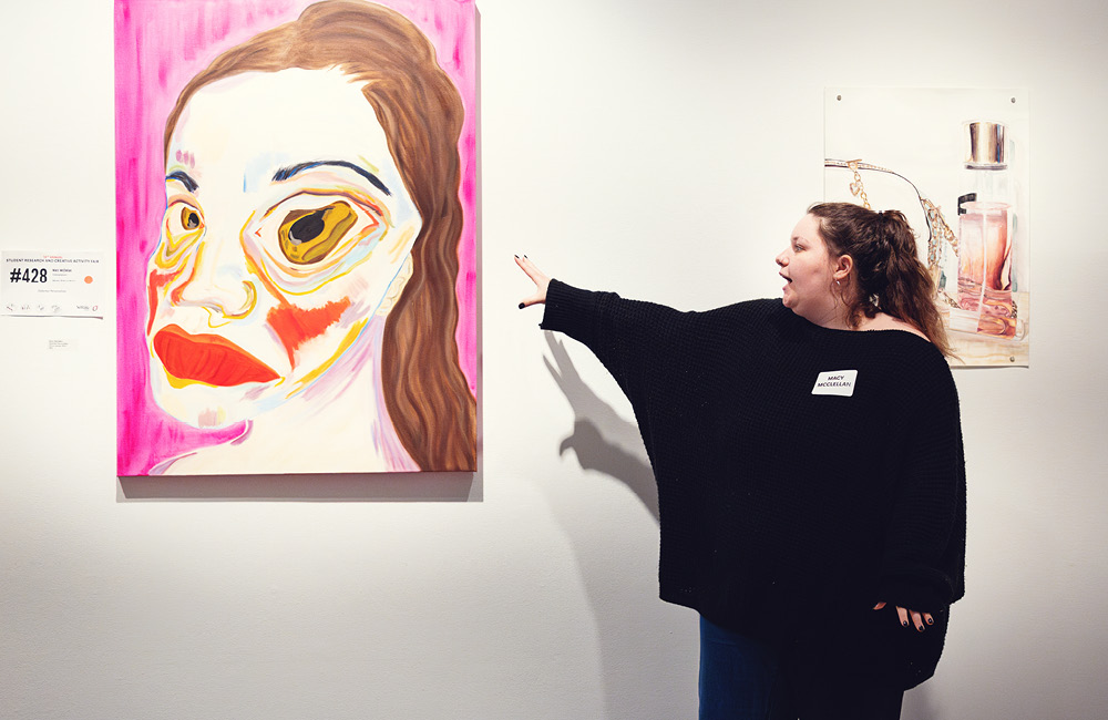 A student presents their artwork at the research and creative activity fair.