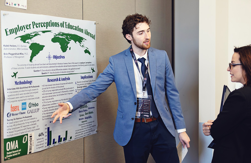 A student stands beside a poster on employer perceptions and discusses their findings.