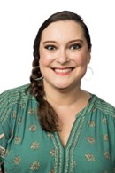 A smiling woman with her hair in a braid, wearing hoop earrings and a teal-patterned blouse.