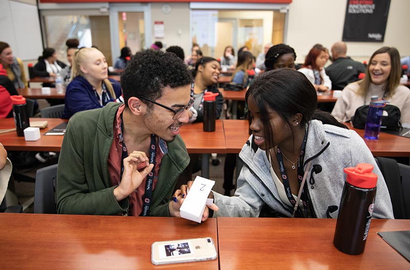 two students of color sit at a table and talk.