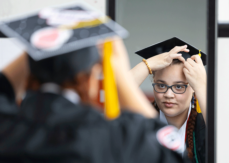 a woman fixes her mortar board in a mirror