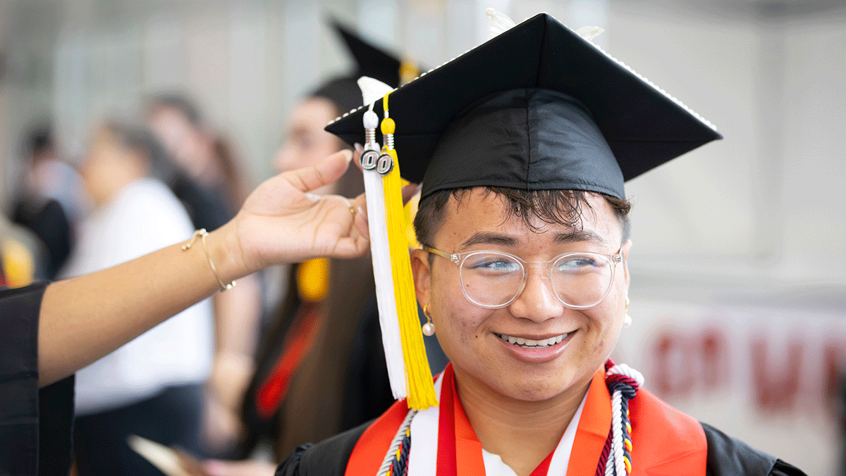 a man of color smiles as a yellow and white tassel hangs off of his mortar board