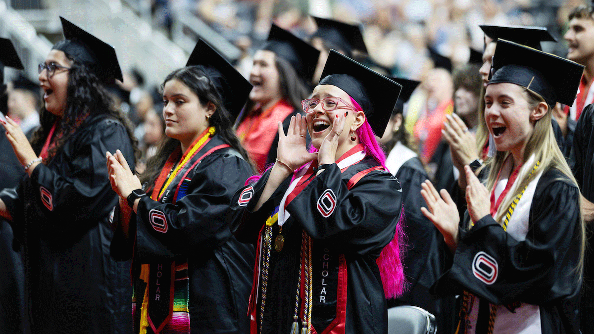 a group of female graduates, one with bright pink hair, cheer excitedly at uno's commencement