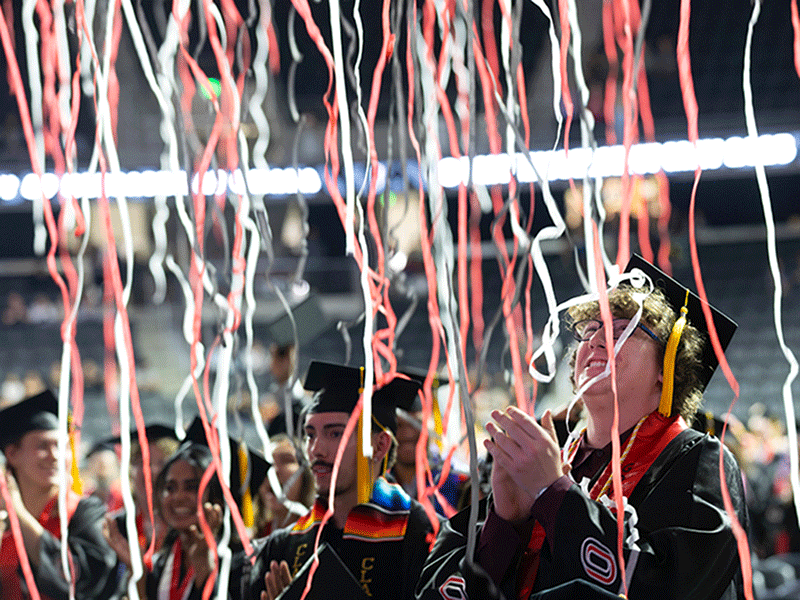 students celebrate under red, white, and black confetti att he end of uno's commencement ceremony