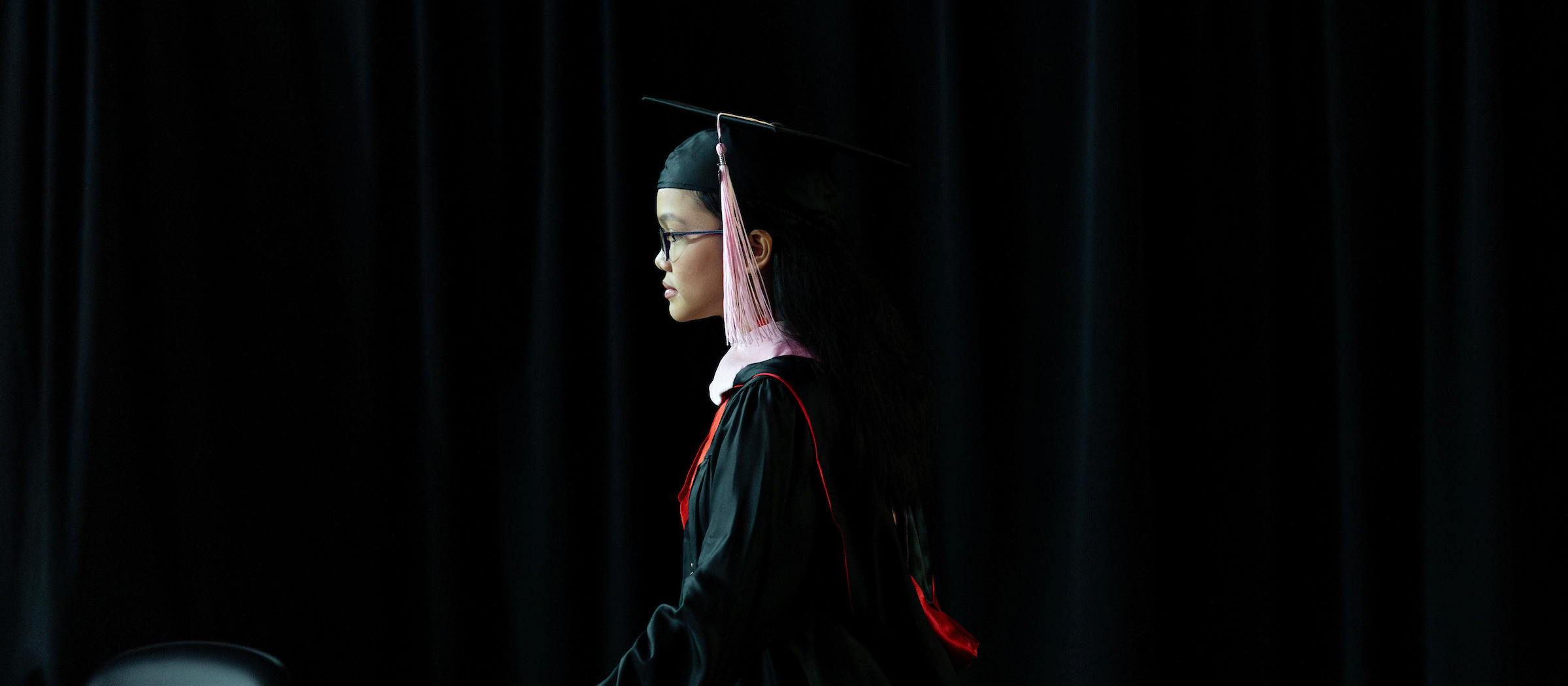 a young asian woman walks across the commencement stage