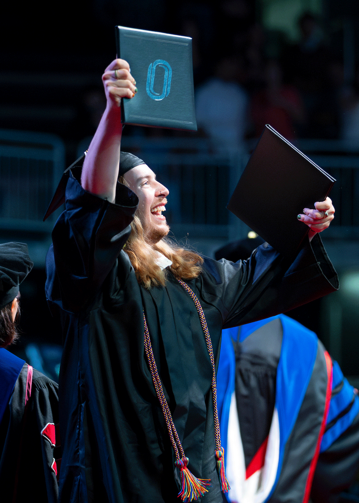 a graduate proudly shows off their diploma on stage at uno's commencement 