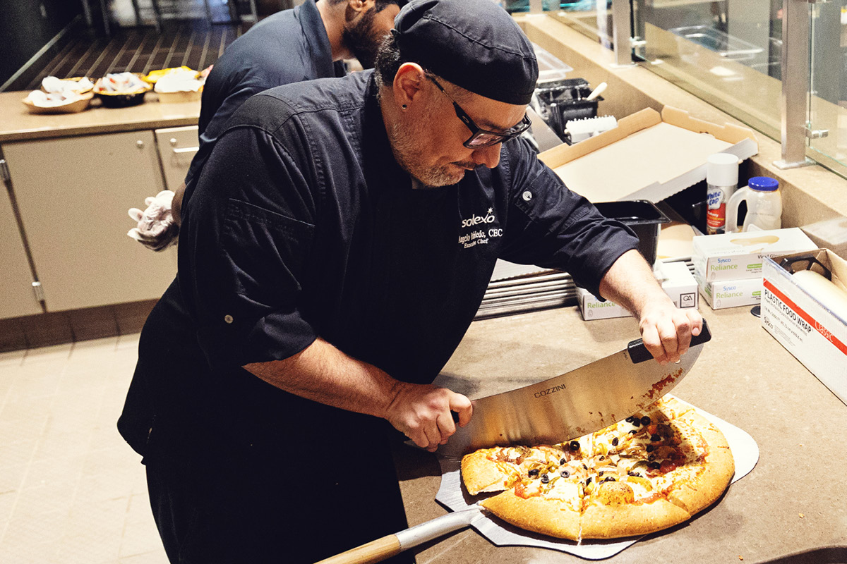 UNO dining staff member slices a freshly baked pizza in the campus kitchen.