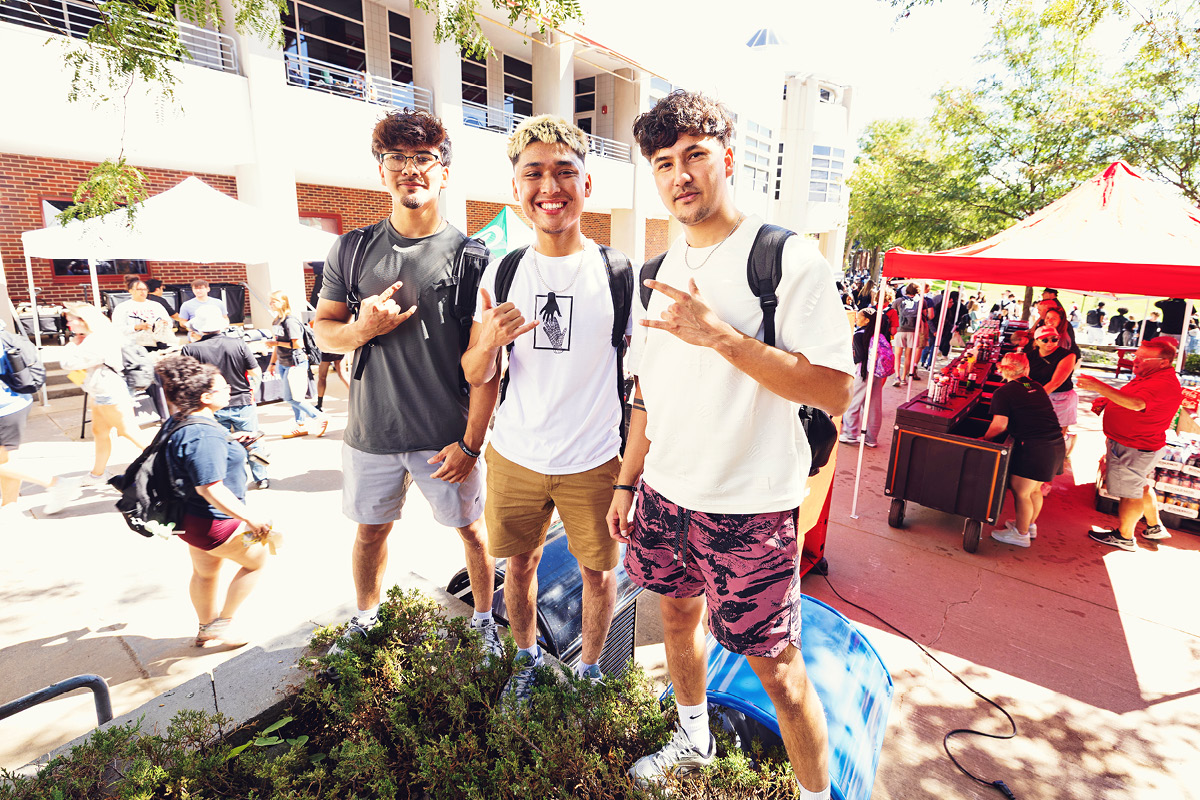 Three students pose together and smile during an outdoor campus event.