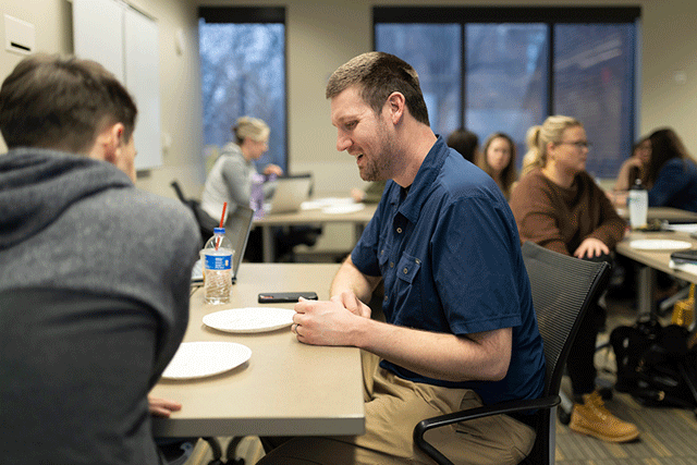 A university student smiles while participating in a classroom discussion with peers.