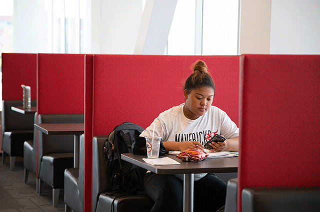 a female student sits at a table looking at her phone.