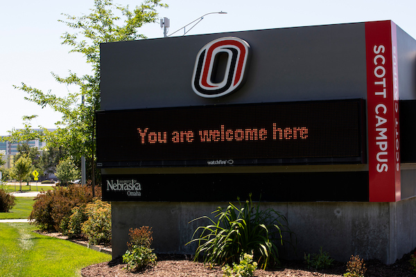 University of Nebraska at Omaha Scott Campus sign displaying “You are welcome here” with campus landscaping and greenery in the foreground.