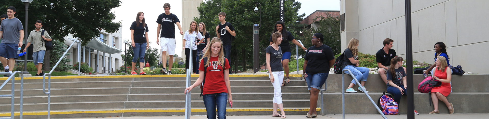 A group of college students is gathered on outdoor steps in front of a campus building, some standing and some sitting with backpacks. Across the center of the image, a black transparent banner displays the text "Office of Student Legal Services" and "Free Legal Support for UNO Students." The scene conveys a welcoming and casual campus atmosphere, promoting accessible legal services for students.