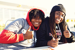 Two students looking into the camera with thumbs up