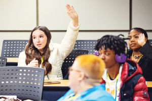 Student sin classroom with one holding her hand up to ask a question.