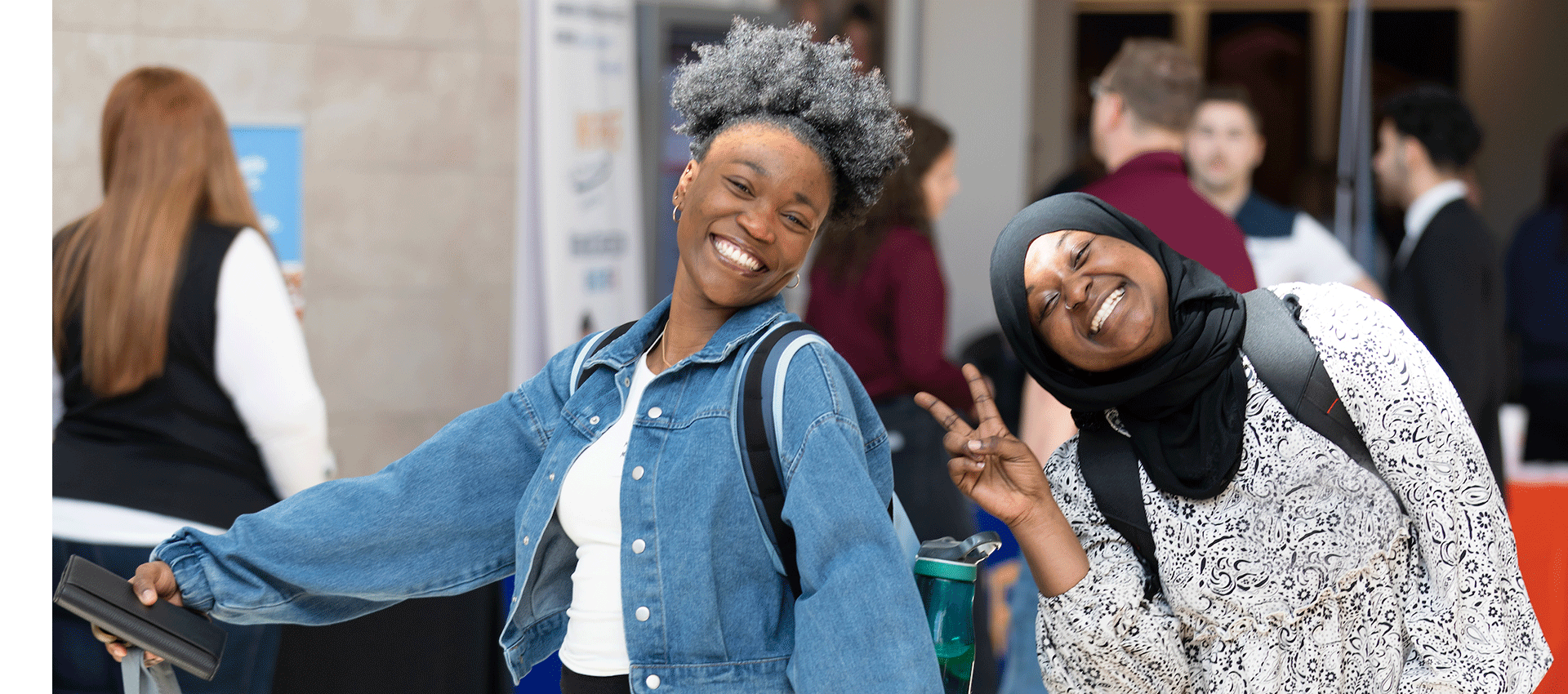 2 women of color smile and show the peace sign.
