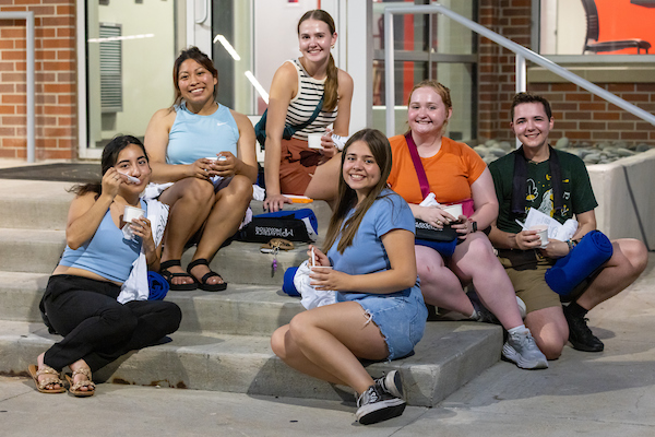 UNO students sit together on some stairs, smiling and enjoying movie night