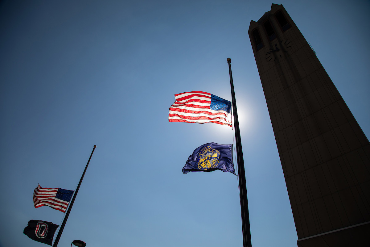 American, state, and UNO flags are lowered by the campanile