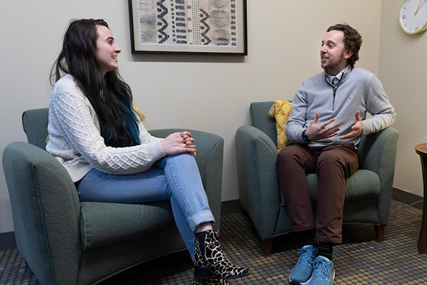a man and woman sit in chairs talking to each other